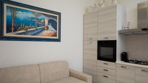 A modern kitchen with a built-in oven and stove, a beige sofa, and a painting of a coastal landscape. - Casa Perla by Wonderful Italy (Olbia)