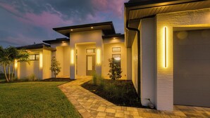 Un moderno edificio residencial con entrada pavimentada, varios accesos e iluminación exterior.