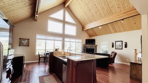 Een ruime keuken met een groot eiland, houten plafond en grote ramen.