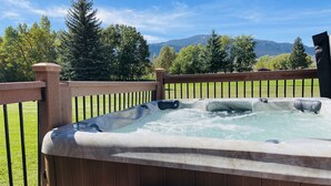 Een hottub op een houten terras met uitzicht op bergen en bomen.