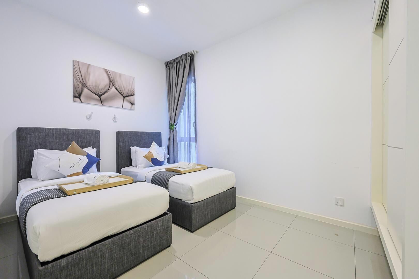 Een hotelkamer met twee bedden, een groot raam met gordijnen, een kunstwerk aan de muur en een schoon, betegeld vloer.
