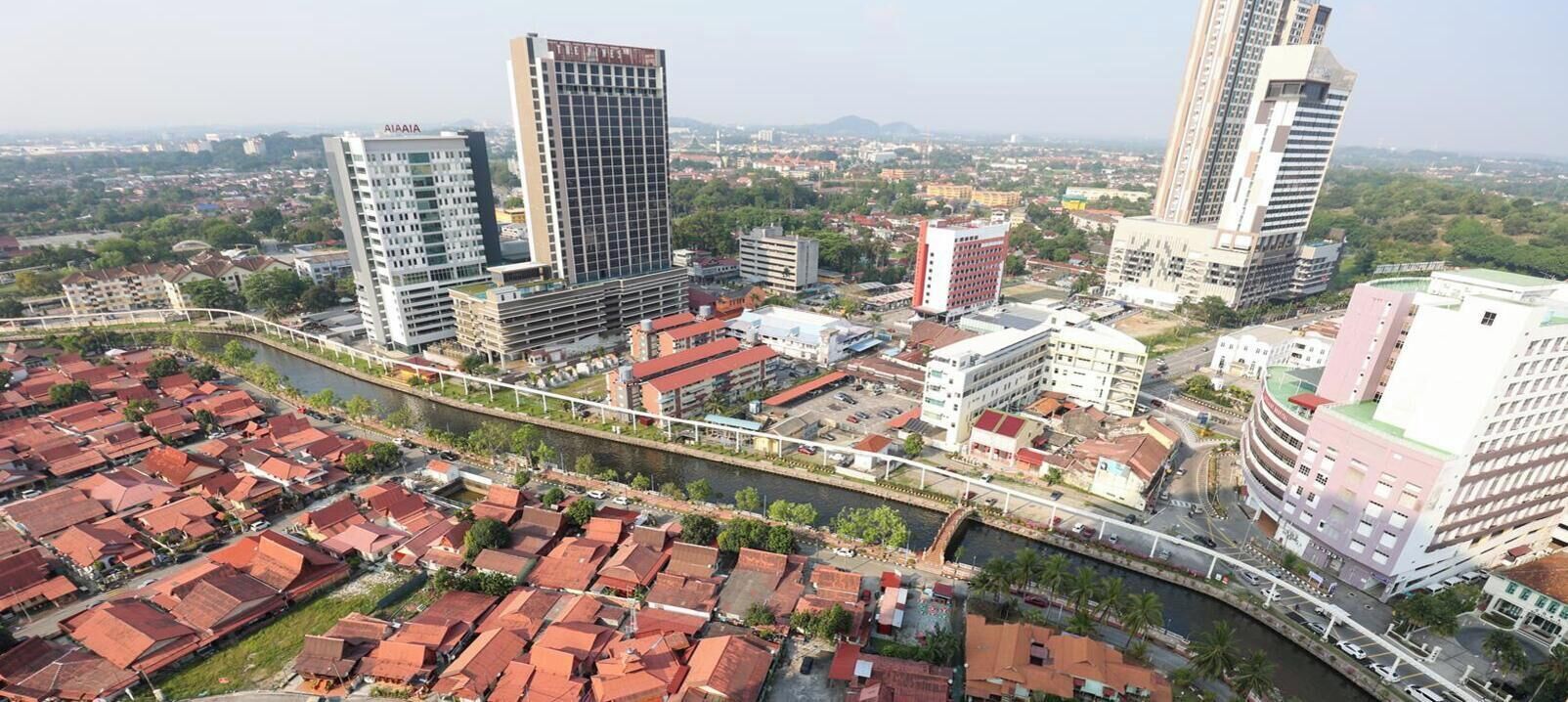 Un paisaje urbano con modernos rascacielos, un río y casas tradicionales con tejados rojos.