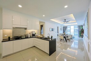A modern kitchen with white cabinetry, a black countertop, and a dining area with a table and chairs. - The Shore Residence Melaka By I Housing (Malacca City)
