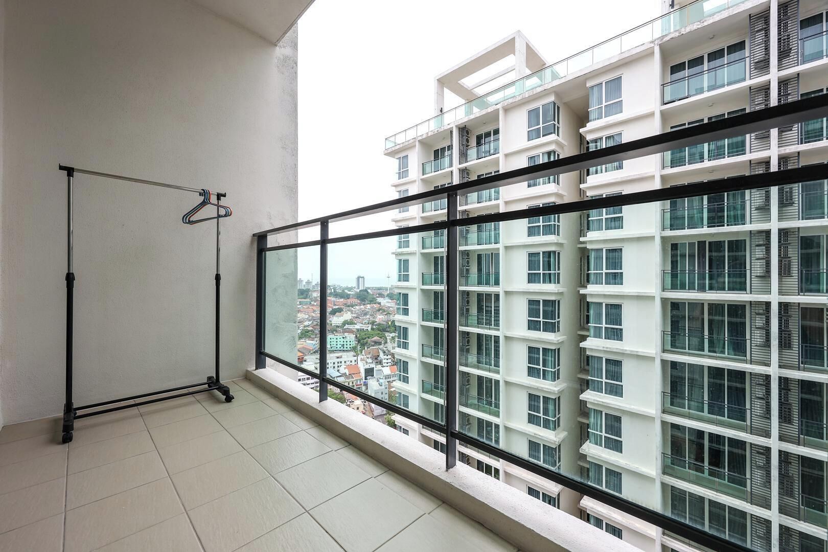 A balcony with a metal rack, a tiled floor, and a view of a multi-story building with balconies.