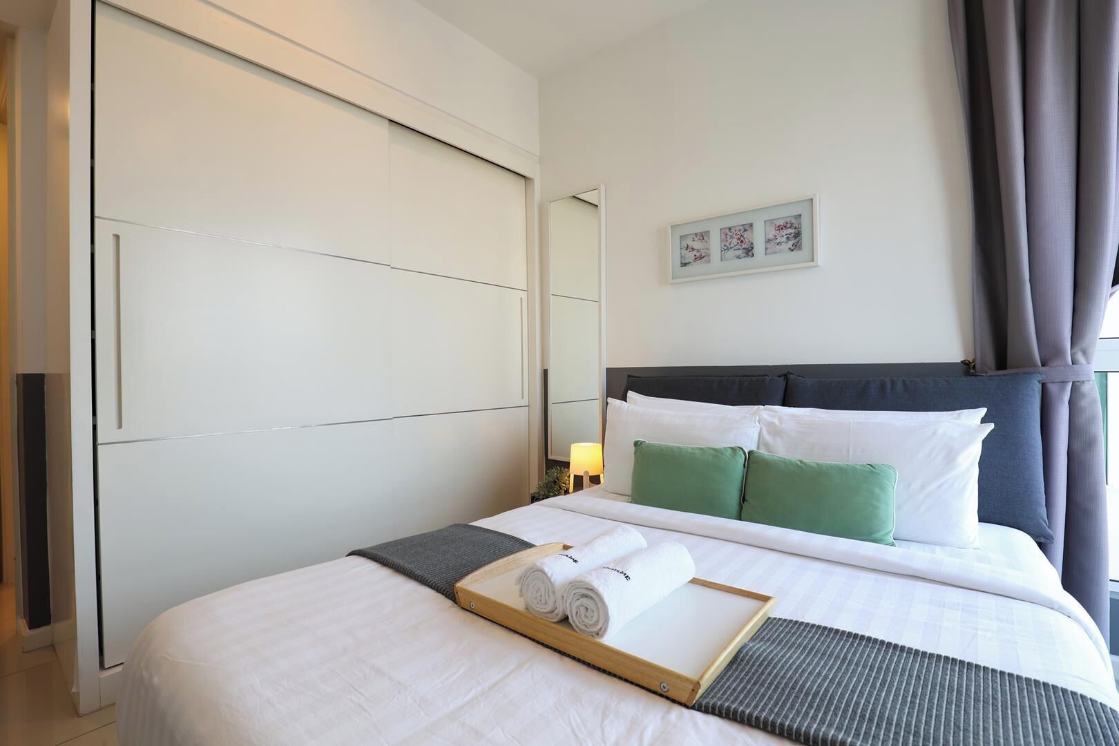 A hotel room with a large bed, a bedside table with a lamp, and a view of the outdoors.