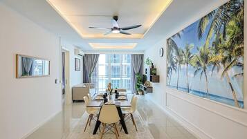 A modern dining area with a ceiling fan, a large window with curtains, and a painting of palm trees.