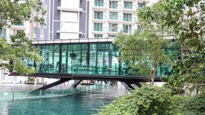 A modern building with a glass facade, a bridge over water, and lush greenery. - The Shore Residence Melaka By I Housing (Malacca City)