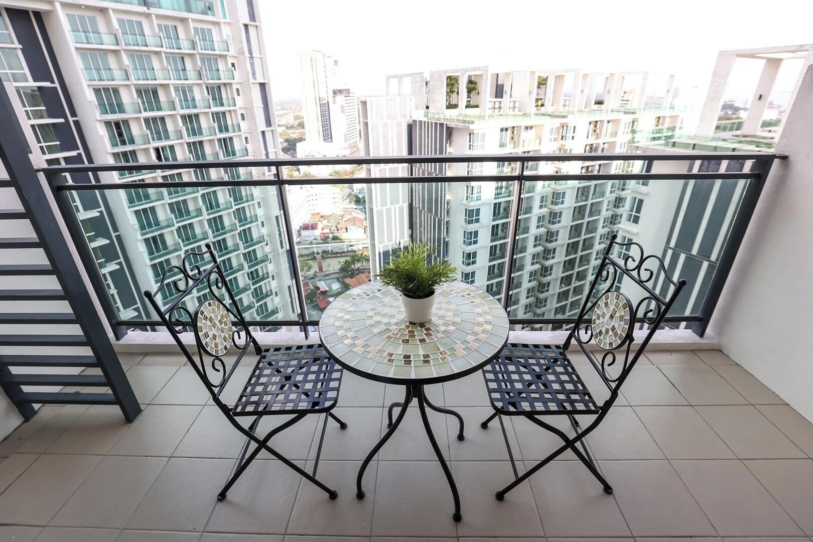 A balcony with a glass table and chairs, a potted plant, and a view of high-rise buildings.