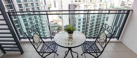 A balcony with a glass table and chairs, a potted plant, and a view of high-rise buildings.