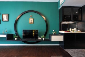 A modern living room with a flat-screen TV, a circular wall decoration, and a kitchen area with cabinets and a countertop. - The Shore Residence Melaka By I Housing (Malacca City)