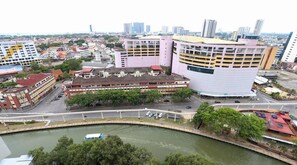 Eine Stadtansicht mit einem markanten, pinkfarbenen Gebäude mit außergewöhnlicher, geschwungener Architektur, umgeben von weiteren Gebäuden und einem Fluss mit einer Brücke.