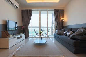 A modern living room with a sofa, a flat-screen TV, a dining table, and a balcony with a view. - The Shore Residence Melaka By I Housing (Malacca City)