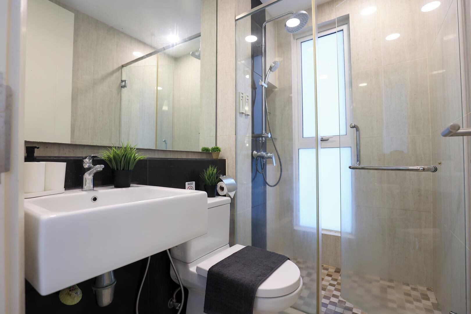 Un baño moderno con ducha envuelta en vidrio, un lavamanos blanco y un inodoro.