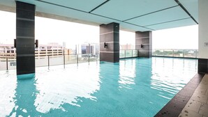 An indoor swimming pool with clear water, surrounded by walls and pillars, with a view of buildings in the background. - The Shore Residence Melaka By I Housing (Malacca City)