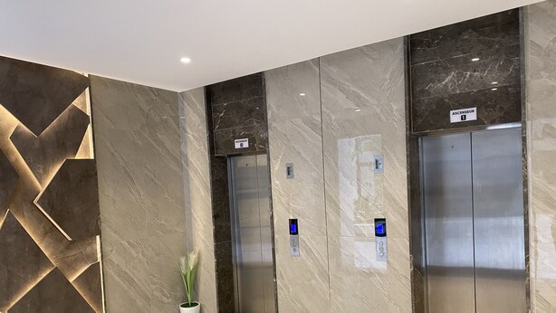 A modern elevator area with marble walls, a geometric light feature, and a potted plant. - Résidence nirvâna  (Sousse)