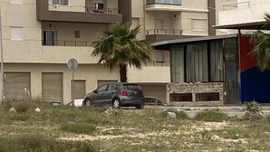 A multi-story residential building with balconies, a parked car, and a palm tree in the foreground. - Résidence nirvâna  (Sousse)