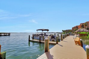 A wooden dock leading to a marina with boats and a thatched-roof structure.