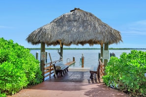 A wooden dock leading to a thatched-roof gazebo by a calm lake.