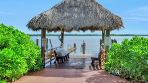 Un molo di legno conduce a un gazebo con tetto di paglia affacciato su un lago tranquillo.