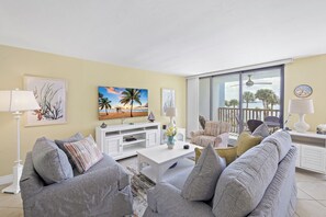 A living room with striped sofas, a white entertainment unit, and a painting of a beach scene. - Riverfront condo in Olde Marco | Pools/Tennis (Marco Island)