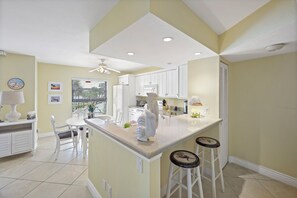 A kitchen with white cabinets, a dining area with a table and chairs, and a bar area with stools. - Riverfront condo in Olde Marco | Pools/Tennis (Marco Island)