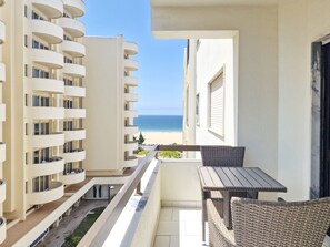 A balcony with a view of the beach, a table, and wicker chairs. - Apartment Praia Rocha | River View | Colunas (Portimão)