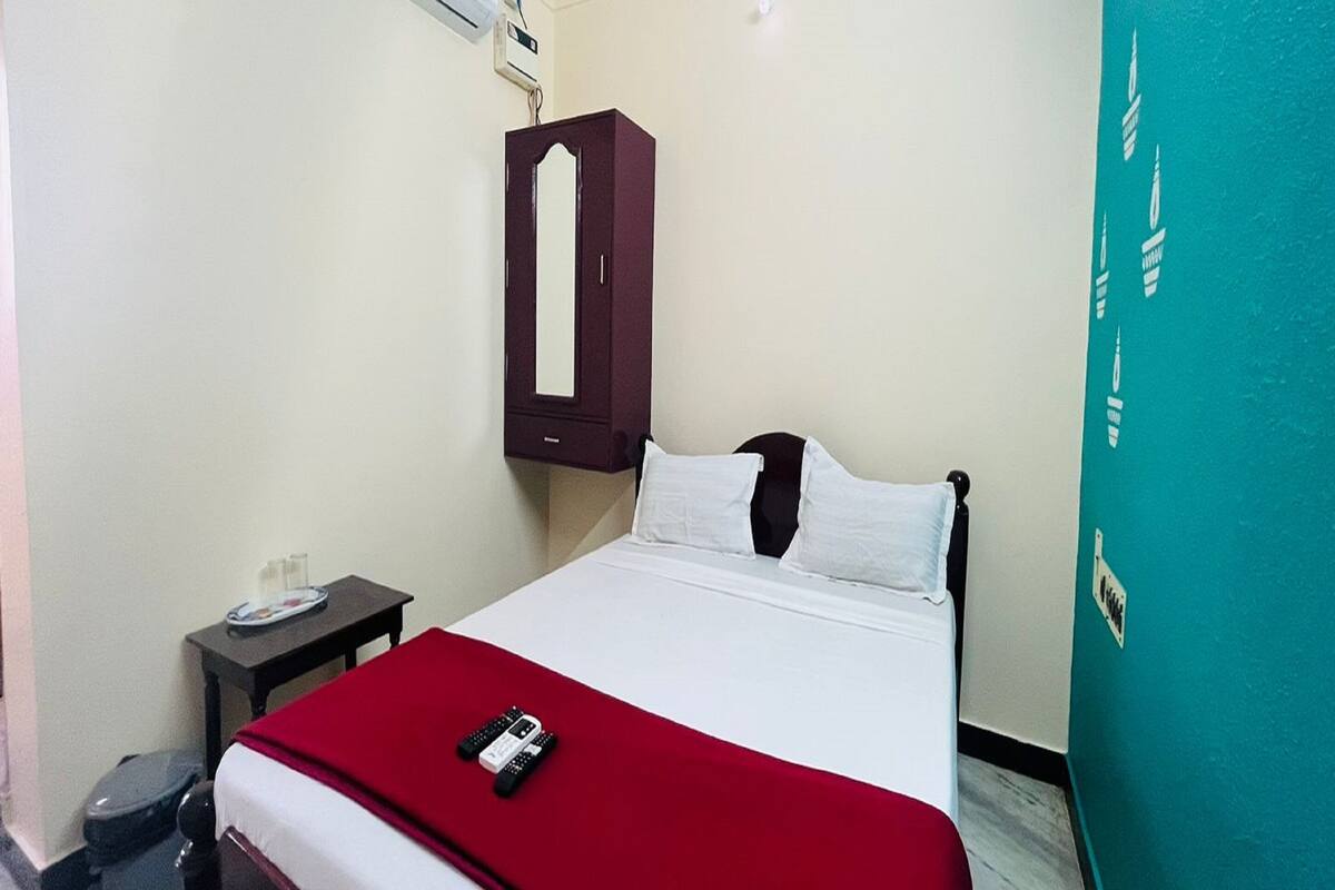A hotel room with a bed, a nightstand, a red blanket, and a wardrobe.