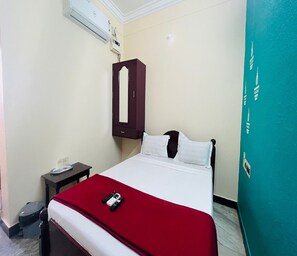 A hotel room with a bed, a nightstand, a red blanket, and a wardrobe.