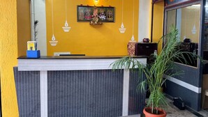 Un comptoir d’accueil avec un mur jaune, un tableau encadré au-dessus et une plante en pot à côté.