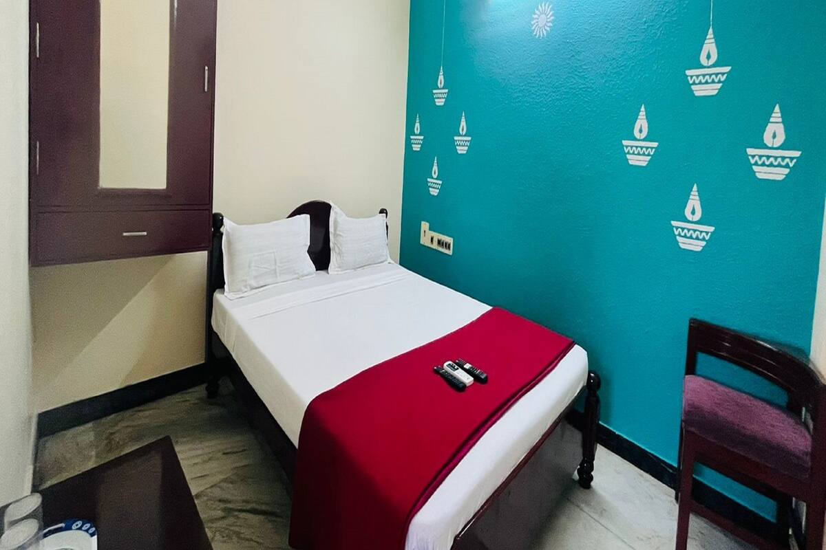 A bedroom with a bed, a chair, a mirror, and a wall with decorative lights.