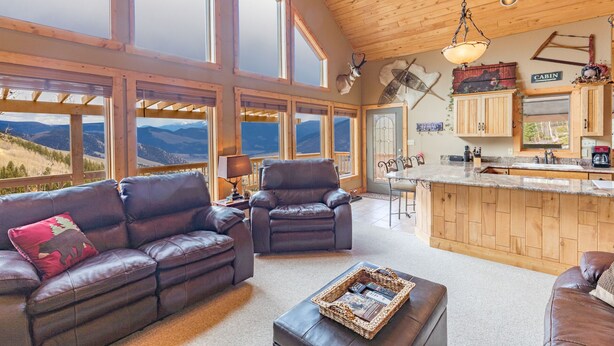 A spacious living area with leather sofas, a coffee table, and a kitchen with wooden cabinets and a bar.