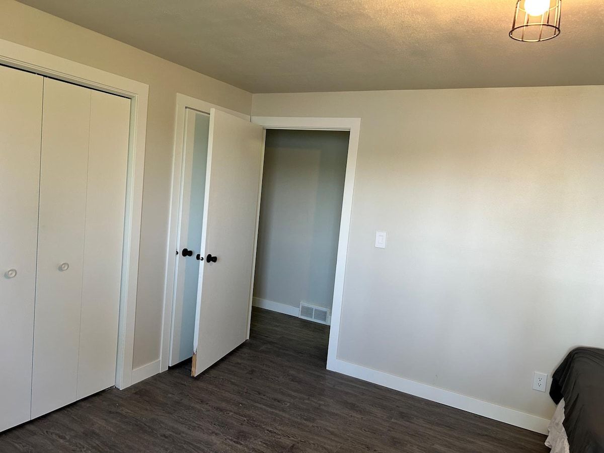 A room with a wooden floor, white walls, and a door leading to another room.