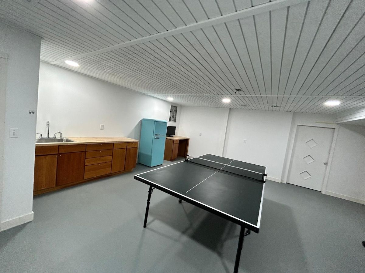 A room with a ping pong table, wooden cabinets, a blue cabinet, and a white door.