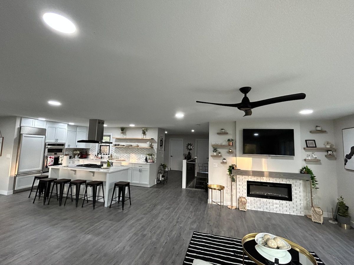 A modern kitchen with a central island, bar stools, and a dining area with a TV mounted on the wall.