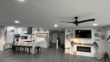 A modern kitchen with a central island, bar stools, and a dining area with a TV mounted on the wall.