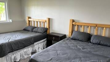 Une chambre avec deux lits, chacun doté d’une tête de lit en bois et d’une literie grise. Une petite table de chevet avec un tiroir se trouve entre les deux lits.