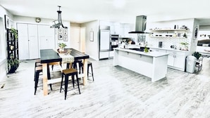 Een moderne keuken met witte kasten, een centraal eiland en een eethoek met een zwarte tafel en houten stoelen.