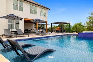 A swimming pool with lounge chairs and umbrellas, a covered seating area, and a building with large windows. - Spa/Pool, GameBarn, Pickleball, FirePit, Big Views (Driftwood)