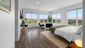Un dormitorio con cama, escritorio, silla y ventanas amplias.
