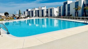 Et moderne hotel med et rektangulært poolområde, liggestole og en klar, blå himmel.