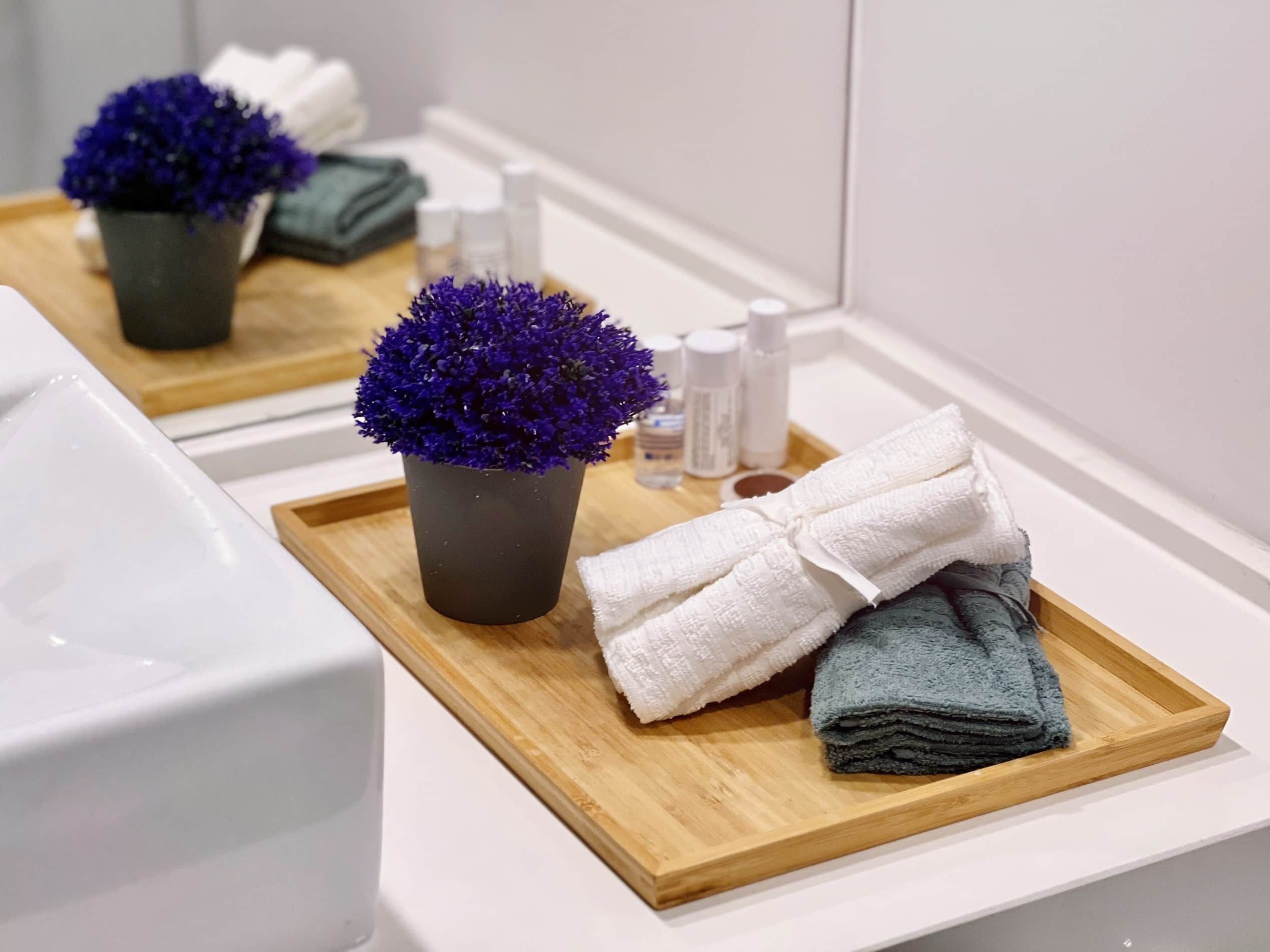 Une salle de bain avec un plateau en bois sur lequel sont posés un pot de fleurs, des serviettes et des articles de toilette.