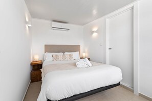 A bedroom with a bed, bedside tables, an air conditioning unit, and a door.