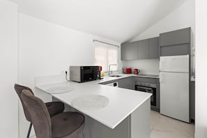 A modern kitchen with a white island, grey cabinets, a built-in oven, and a stainless steel refrigerator.