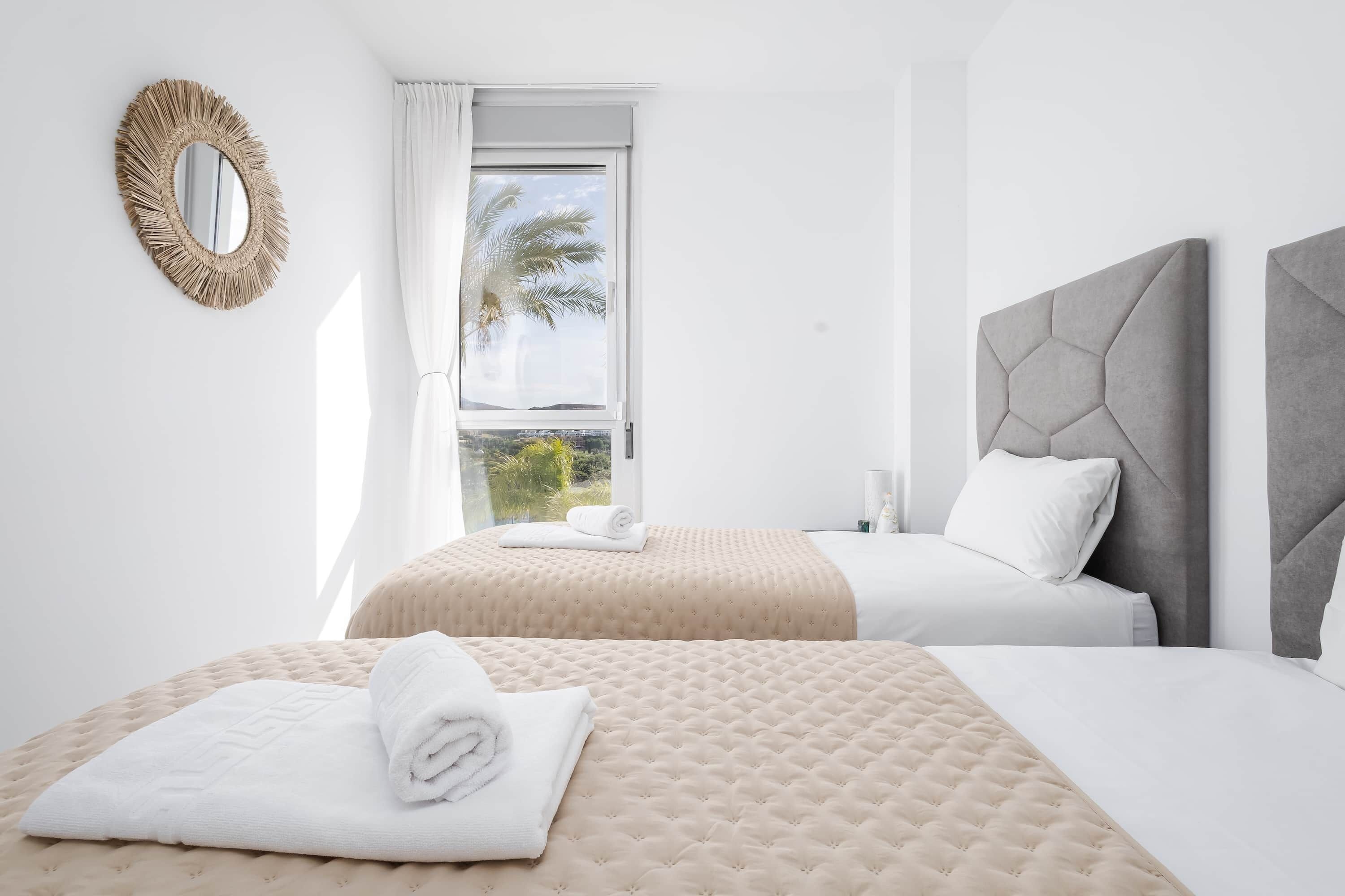 Een hotelkamer met twee bedden, een grote spiegel en een raam met uitzicht op palmbomen.