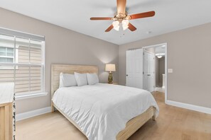 A bedroom with a bed, a ceiling fan, a nightstand, a lamp, and a door leading to another room. - Walk to Beach - 4BR Surfside Beach Home w/ Private Pool & Beach Access (Surfside Beach)