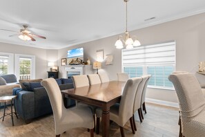 A dining area with a wooden table, beige upholstered chairs, a ceiling fan, and a television on the wall.