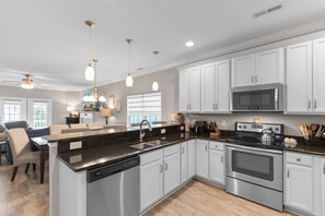 A modern kitchen with white cabinets, stainless steel appliances, and pendant lighting.