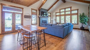 A spacious living area with a wooden ceiling, a large sofa, a dining table with stools, and a fireplace. - Family Getaway with Access to Exclusive Golf (Sunriver)