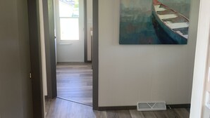 Un corridoio con pavimento in legno, una plafoniera e un quadro raffigurante una barca al muro.