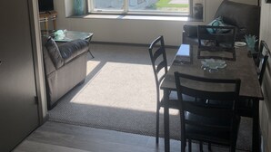 Un ambiente compatto con angolo pranzo, divano, televisione e finestra vista su una casa e alberi.